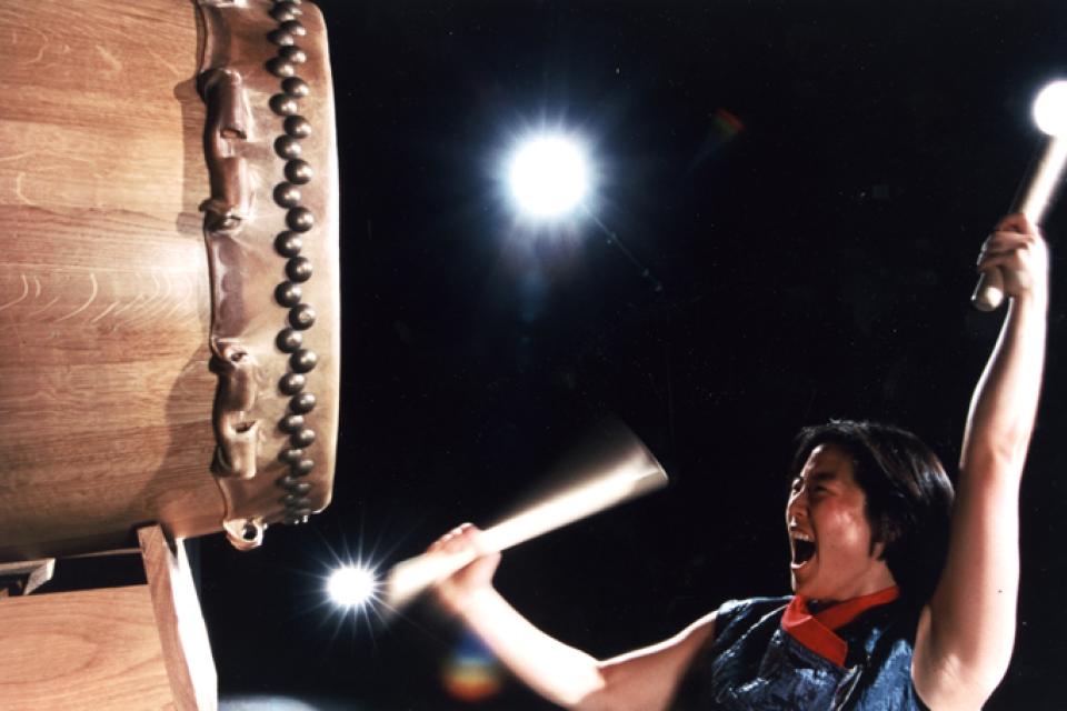 Ann Ishimaru with eyes closed and mouth open in mid drum beat